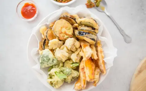 Chrupiące warzywa w cieście tempura: bakłażan, brokuły i marchewka, podane z sosem.