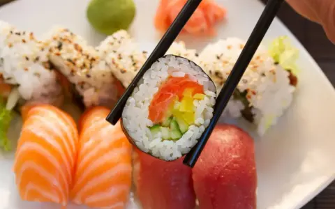 Pyszna rolka sushi z łososiem, ogórkiem i papryką, trzymana pałeczkami. Zastanawiasz się, ile waży rolka sushi?