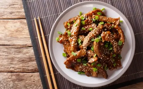 Pyszne kawałki wołowiny w sosie teriyaki, posypane sezamem i szczypiorkiem, gotowe do podania z pałeczkami.