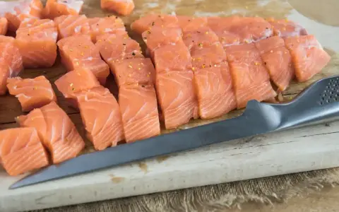 Pokrojona w kostkę i plastry świeża ryba do sushi, przyprawiona, leży na desce obok noża.