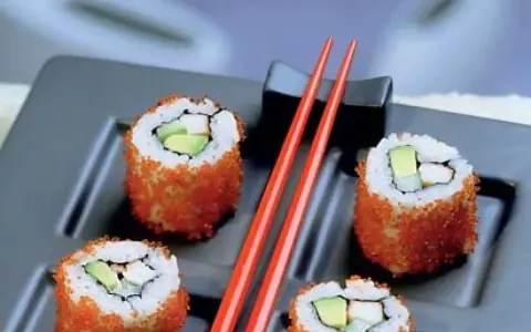Cztery rolki sushi z awokado i rybą, obtoczone pomarańczową ikrą. Idealne sushi na diecie, podane z czerwonymi pałeczkami.