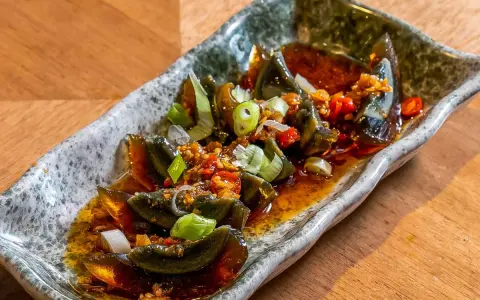 Kawałki 100 letniego jajka w pikantnym sosie z czosnkiem, chili i szczypiorkiem na kamiennej tacy.