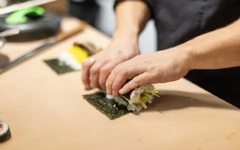 Dłonie zwijają sushi na arkuszu nori, ukazując jego wszechstronne właściwości kulinarne.