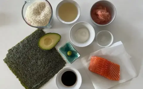 Wszystkie składniki do sushi: ryż, nori, łosoś, awokado, sos sojowy, wasabi, imbir marynowany, ocet ryżowy i sól.