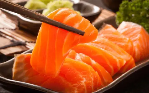 Sashimi co to? Świeży łosoś, chwytany pałeczkami, podany z wasabi i natką pietruszki.