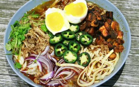 A miseczce ramen z wieprzowiną, jajkiem na pół, papryczkami jalapeño, cebulą i kolendrą.