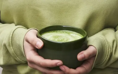 Dłonie trzymające zieloną miseczkę z pianką matcha.