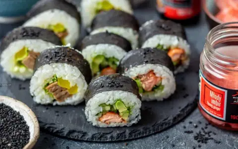 Pyszne sushi z łososiem, awokado i ogórkiem, posypane czarnym sezamem. Obok słoiczek marynowanego imbiru.