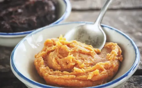 Pomarańczowa pasta miso w miseczce, obok ciemniejsza pasta. Łyżeczka zanurzona w jasnej paście.