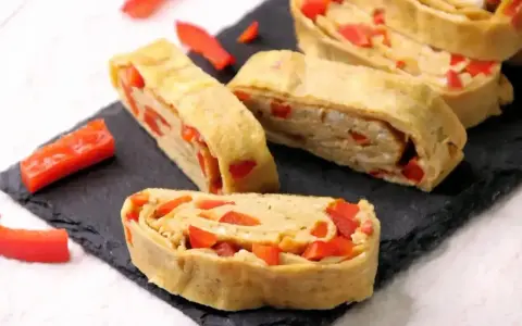 Roladki z jajek z papryką, przypominające omlet do sushi, ułożone na czarnej desce.