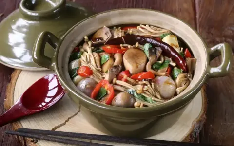 Gęsta zupa z grzybkami mun, enoki, pieczarkami, papryczkami chili i cebulką, podana w glinianym garnku.