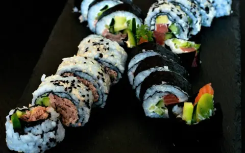 Pyszne rolki sushi z tuńczykiem i awokado, posypane sezamem. Idealna rzepa do sushi na czarnej desce.