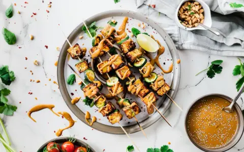 Pyszne szaszłyki z tofu satay, polane kremowym sosem orzechowym, z dodatkiem cukinii i limonki.