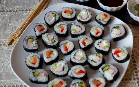Talerz pełen sushi, w tym futomaki tamago z łososiem, awokado i paluszkami krabowymi.
