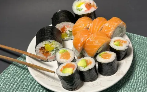 Talerz pełen sushi z łososiem i awokado. Wśród nich rolka z kremowym serkiem do sushi, idealna na przekąskę.
