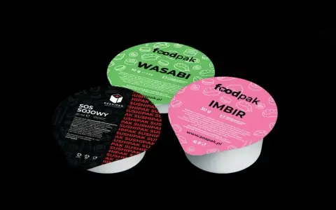 Trzy małe pojemniki z dodatkami do sushi: zielony z wasabi, różowy z imbirem i czarny z sosem sojowym.