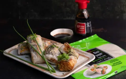 Pyszne sushi w papierze ryżowym, posypane sezamem, podane z sosem sojowym. Obok opakowanie papieru ryżowego.