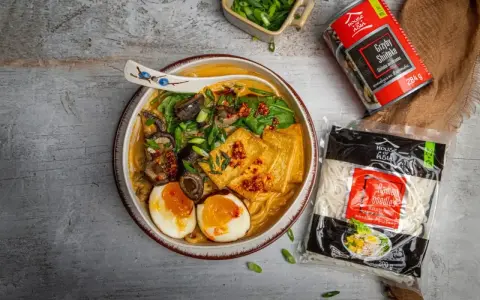 Aromatyczny ramen wołowy z tofu, jajkiem i grzybami shiitake. Obok opakowanie makaronu ramen.