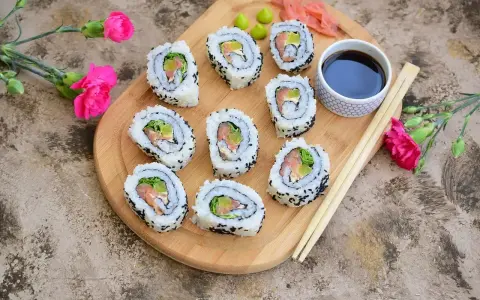 Pyszne california sushi z łososiem i awokado, posypane czarnym sezamem, podane z sosem sojowym i wasabi.
