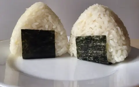 Dwa pyszne onigiri sushi, uformowane w trójkąty i ozdobione kawałkami nori, leżą na białym talerzu.