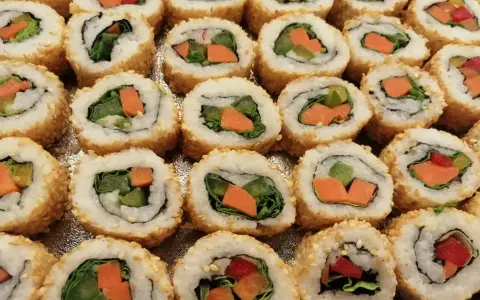 Roladki sushi z sezamem, w środku zielona sałata i pomarańczowa marchewka do sushi.