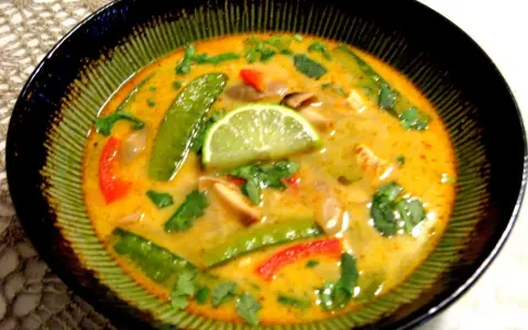 Aksamitna zupa tom kha z kurczakiem, z zielonym groszkiem, papryką i plasterkiem limonki.
