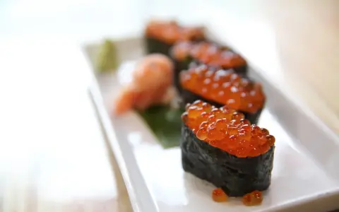 Pięć kawałków sushi z kawiorem, podanych na białym talerzu z odrobiną wasabi i marynowanego imbiru.
