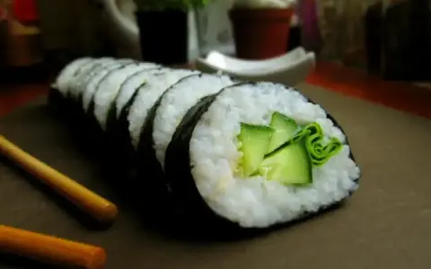 Świeży ogórek do sushi, zwinięty w rolkę z ryżem i nori. Obok leżą pałeczki.