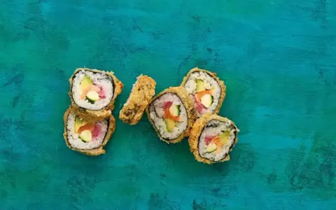 Chrupiące sushi w panierce z łososiem, awokado i ogórkiem na turkusowym tle.