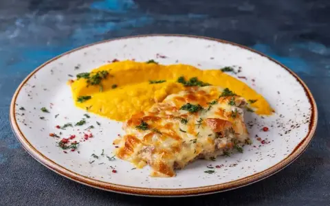 Pyszny katsu z kurczaka zapieczony z serem, podany z purée z dyni i posypany ziołami.