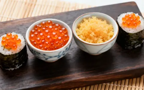 Dwa sushi rolki z pomarańczowym ikrą masago i miseczki z ikrą.