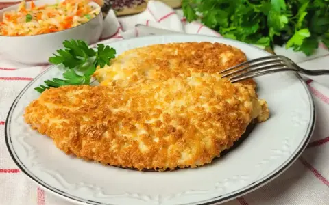 Dwa chrupiące kotlety z kurczaka w panko, podane na talerzu z sałatką z kapusty i marchewki.