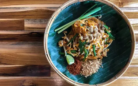 Pyszne pad thai skladniki: makaron ryżowy, kiełki, szczypiorek, orzeszki ziemne, chili i limonka na liściu bananowca.