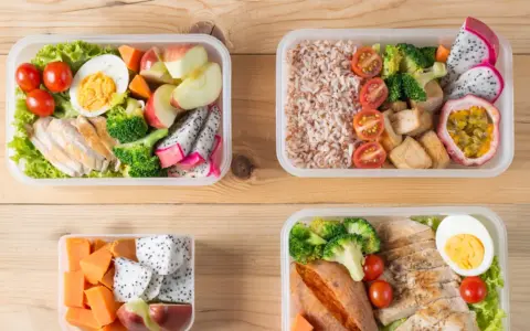 Cztery pudełka bento z kurczakiem, ryżem, warzywami i owocami. Idealne na zdrowy lunch, pokazują, bento co to jest.