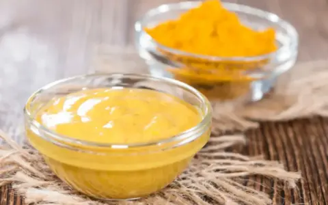 Dwie szklane miseczki na drewnianym tle. Jedna zawiera gładki sos, druga żółtą przyprawę, składniki do korma curry.
