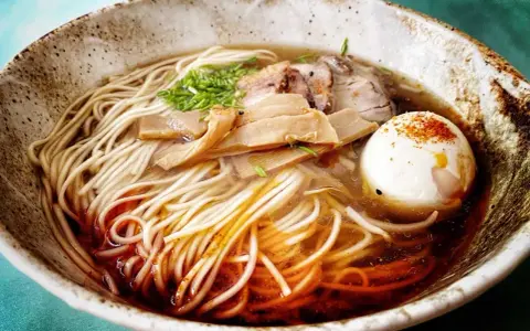 Miseczka aromatycznego ramenu z makaronem, jajkiem, mięsem i bambusem. Widać wyraźnie dodane ramen przyprawy, które nadają daniu głębi smaku.