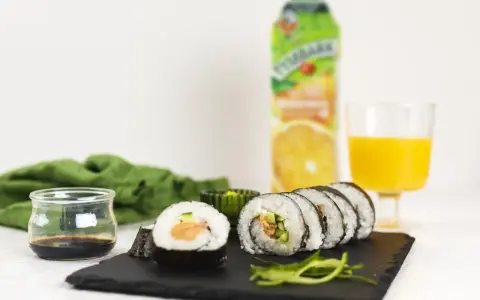 Roladki sushi z surowym łososiem do sushi, ogórkiem i ryżem, podane z sosem sojowym i sokiem pomarańczowym.