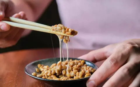 Pałeczki podnoszą lepką masę fasoli. To natto, co to jest? Japoński przysmak o charakterystycznym zapachu i smaku.