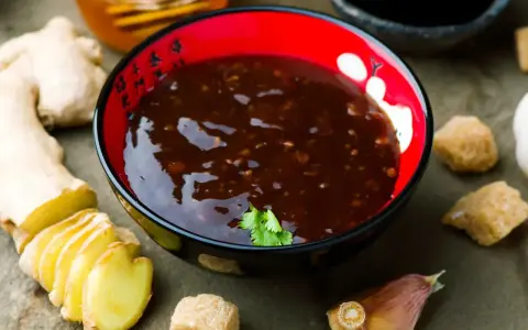 Sos teriyaki przepis: miseczka z ciemnym sosem, obok imbir, czosnek, cukier trzcinowy i miód. Idealny do dań azjatyckich.
