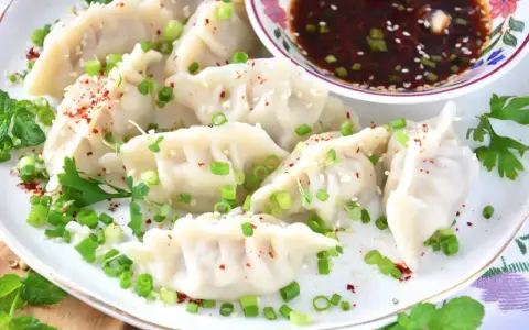 Pyszne pierożki gyoza posypane szczypiorkiem i sezamem, podane z aromatycznym sosem.