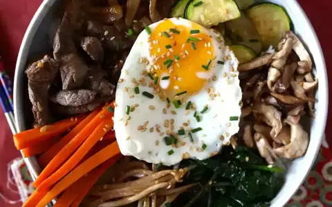 Apetyczne koreańskie dania: bibimbap z wołowiną, warzywami, grzybami i jajkiem sadzonym, posypane sezamem i szczypiorkiem.