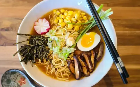 Apetyczne ramen z makaronem, jajkiem na pół, kukurydzą, grzybami shiitake, nori i rzodkiewką. Pyszne danie, które rozgrzewa.
