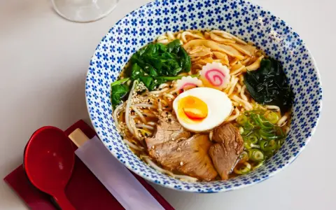 Miseczka aromatycznego makaronu ramen z jajkiem, mięsem, warzywami i kiełkami. Idealny posiłek, który dostarczy energii i zaspokoi głód.
