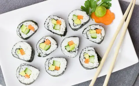Talerz z hosomaki awokado, ogórkiem i marchewką, udekorowany wasabi i natką pietruszki.