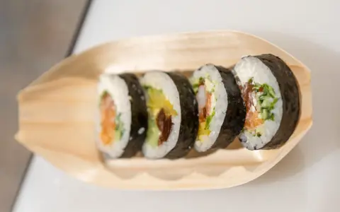 Pięć kawałków sushi z łososiem, awokado i krewetkami na drewnianej łódce. Różne rodzaje sushi nazwy.