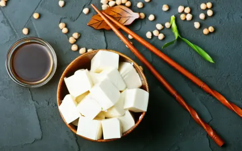 Kostki tofu, czyli przetworzona fasola sojowa, w drewnianej misce, obok sosu sojowego i pałeczek.