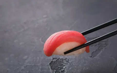 Pałeczki trzymają kawałek sushi z tuńczykiem. Czy sushi jest dobre? Wygląda apetycznie!