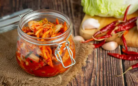 Słoik z kimchi na tle desek, z suszonymi papryczkami chili i czosnkiem.