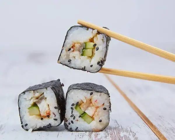 Rolka sushi z ogórkiem i rybą, podniesiona pałeczkami. Zastanawiasz się, ile octu ryżowego na 500g ryżu?
