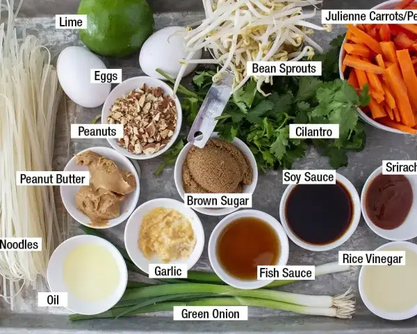 Składniki do sosu pad thai: makaron ryżowy, jajka, orzeszki ziemne, masło orzechowe, olej, czosnek, zielona cebulka, brązowy cukier, kiełki fasoli, kolendra, marchewka, papryka, sos sojowy, sos rybny, ocet ryżowy, sriracha, limonka.
